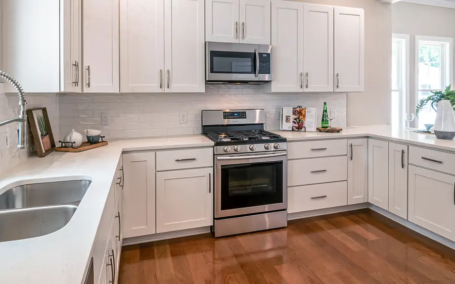 A bright staged kitchen with white cabinets and stone counters